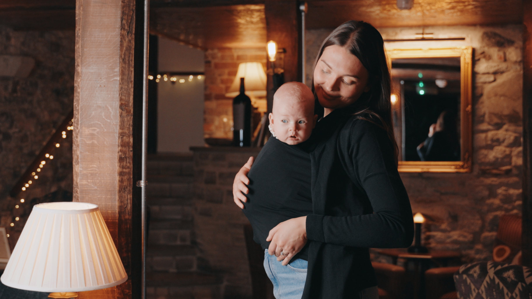 Mother wearing the Alternity Cariagan while carrying her baby in a warm interior